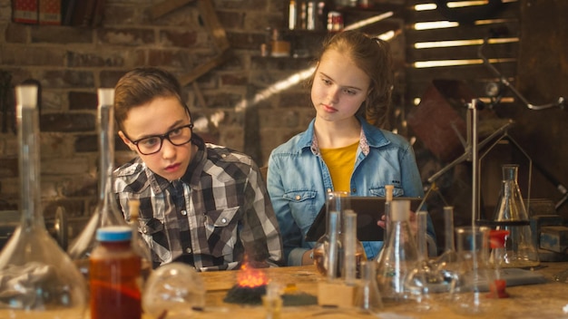 Two female high school students are deeply engrossed in a science experiment, leaning over a lab table filled with equipment and chemicals. They are carefully observing a reaction in a test tube, wearing safety goggles and gloves for protection.
