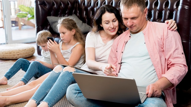 A family sitting together, discussing online safety on a laptop. The parents are pointing at the screen, showing the child various safety settings and privacy controls.