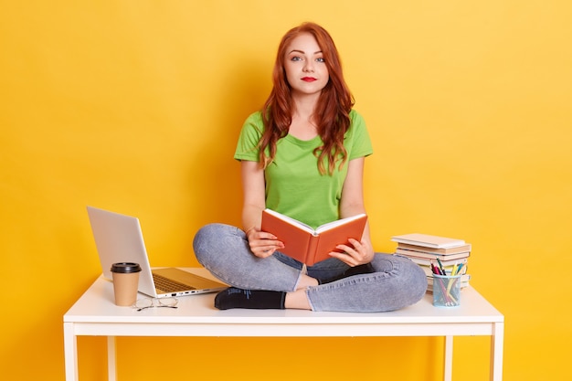 A young girl is sitting at a desk, studying with books and a laptop. Her parents are standing behind her, supporting her and pointing to the computer screen. The image conveys a sense of family support and investment in education.