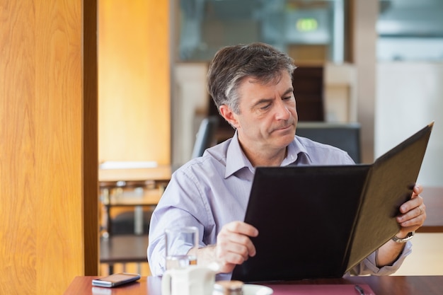 A business owner looking concerned while reviewing financial documents and a spreadsheet on their computer. The setting is a small office, conveying the challenges faced by smaller businesses in managing costs and compliance.