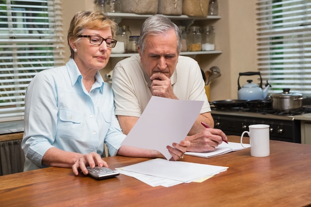 A mature couple sits at a table, reviewing documents related to long-term care insurance. They look concerned as they discuss their options.