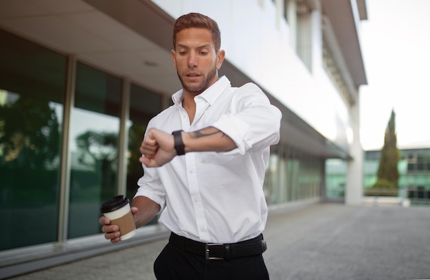 An employee cheerfully using a fitness tracker while walking during a break in a modern office setting.