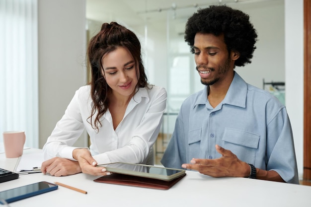 An HR professional explaining the details of a student loan repayment assistance program to a young employee, using a tablet to illustrate the benefits and terms of the program.