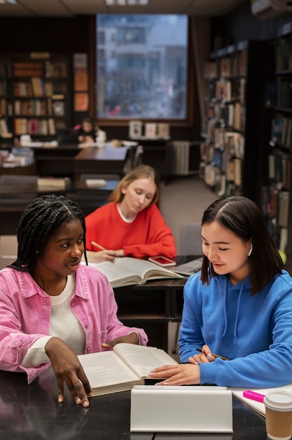 Close-up of a diverse group of college students studying together in a library, with stacks of books and laptops, showing collaborative learning and shared resources, emphasizing community and collective effort in managing college expenses