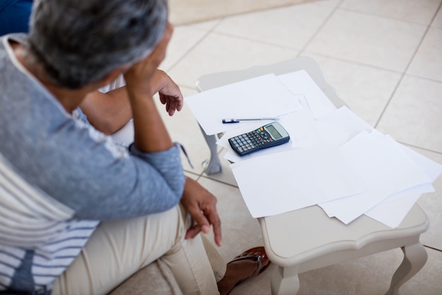 A person looking overwhelmed by a stack of bills and financial statements on their desk, with a calculator and a pen nearby. The scene conveys financial stress and the need for help.