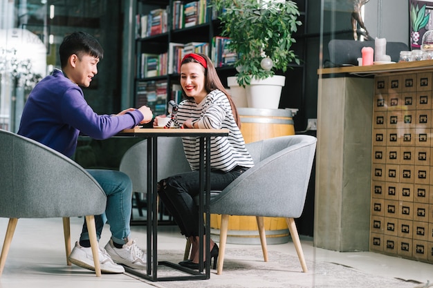 Two people sitting at a table, smiling and shaking hands after a successful meeting. One person is a financial advisor holding a tablet, and the other is a client. The scenario conveys a successful and trusting business relationship.