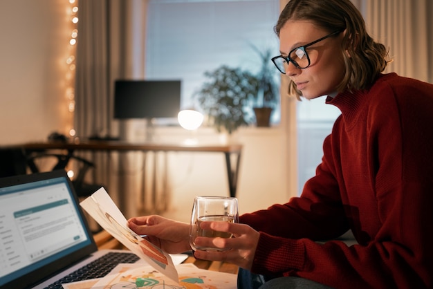 A woman using a laptop at her home office, reviewing financial documents and making notes. A budgeting app is visible on her screen, and she appears focused and determined.