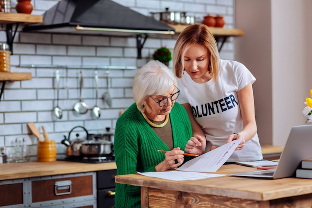 An elderly woman reviewing paperwork with her daughter at a kitchen table, focusing on long-term care insurance policies.