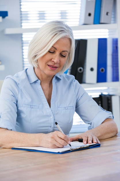 A middle-aged woman reviewing her health insurance policy and medical records at her desk with a calculator and notepad.