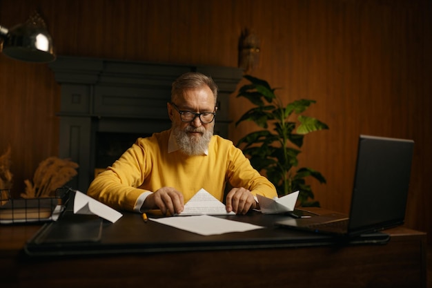 A mature person sitting at a desk reviewing retirement plan documents, with a contented expression. The lighting is warm and inviting, suggesting financial security and peace of mind.