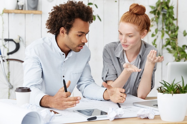 Two people sitting at a table discussing a financial plan. One person is pointing to a financial chart while the other is listening attentively. The setting is bright and modern, suggesting a professional financial advisor meeting.