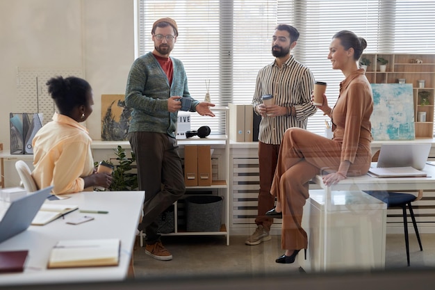 A group of diverse employees collaborating around a table in a modern, open-plan office. There are laptops, notebooks, and coffee cups on the table, indicating a collaborative work session. Natural light and friendly atmosphere.